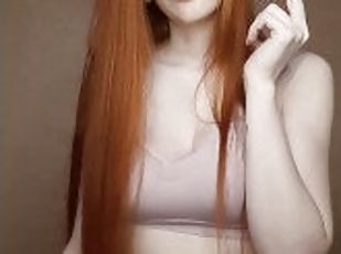 A red-haired girl with long hair smokes a cigarette with a brown filter.